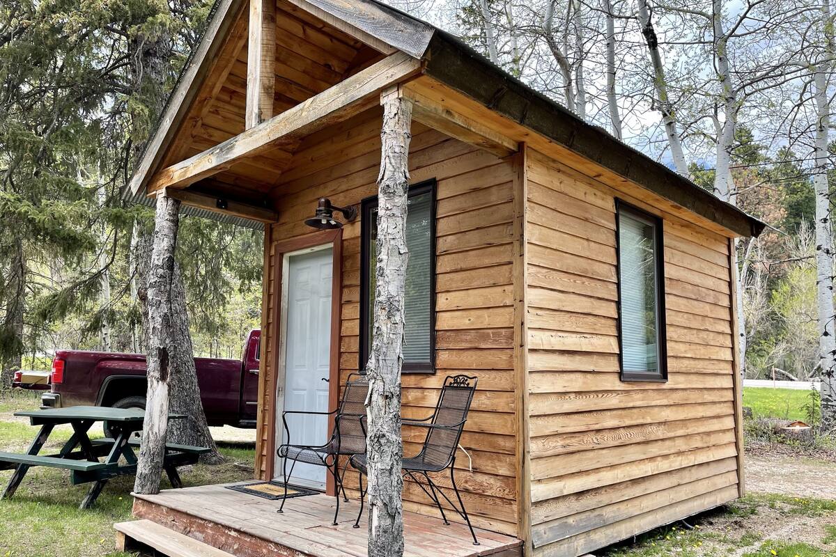 A small wooden cabin with a porch, a door, and two chairs.
