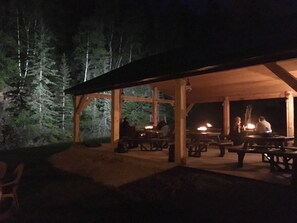An outdoor wooden pavilion with tables and benches, surrounded by trees. - Whitetail Creek Camping Resort (Lead)