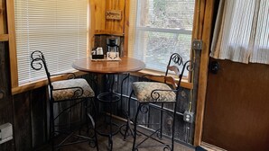 A cozy corner with a wooden table, two chairs, a coffee maker, and a decorative fish sign. - Whitetail Creek Camping Resort (Lead)