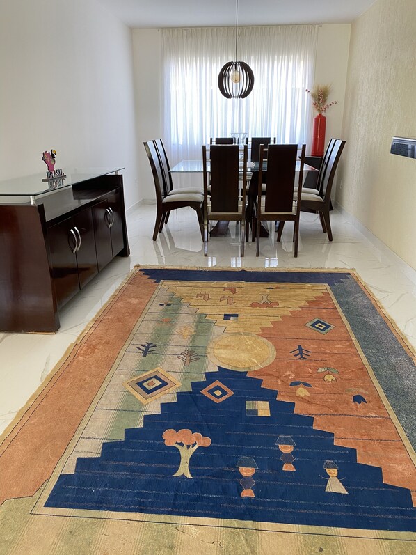 A dining area with a table and chairs, a dark wooden cabinet, and a colorful rug.