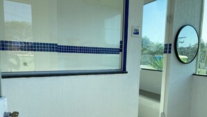Entree van een hotelkamer met een deur, een raam met blauwe betegelde vensterbank, een spiegel en uitzicht.