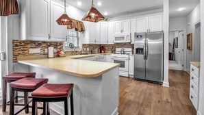 A modern kitchen with white cabinets, a central island with stools, stainless steel appliances, and pendant lighting.