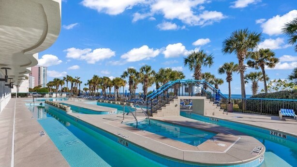 Una piscina con múltiples carriles, palmeras y una escalera que conduce a una terraza.