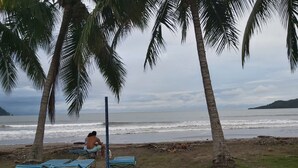 Una playa con palmeras, una zona de arena con sillas de metal azules y vista al océano.