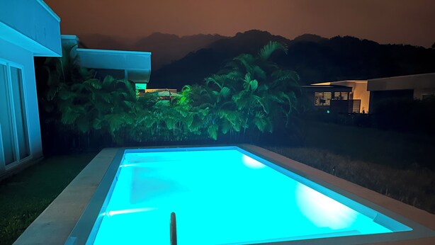 Una piscina con una fuente de agua cristalina azul, rodeada por un jardín ajardinado y vistas a colinas lejanas.