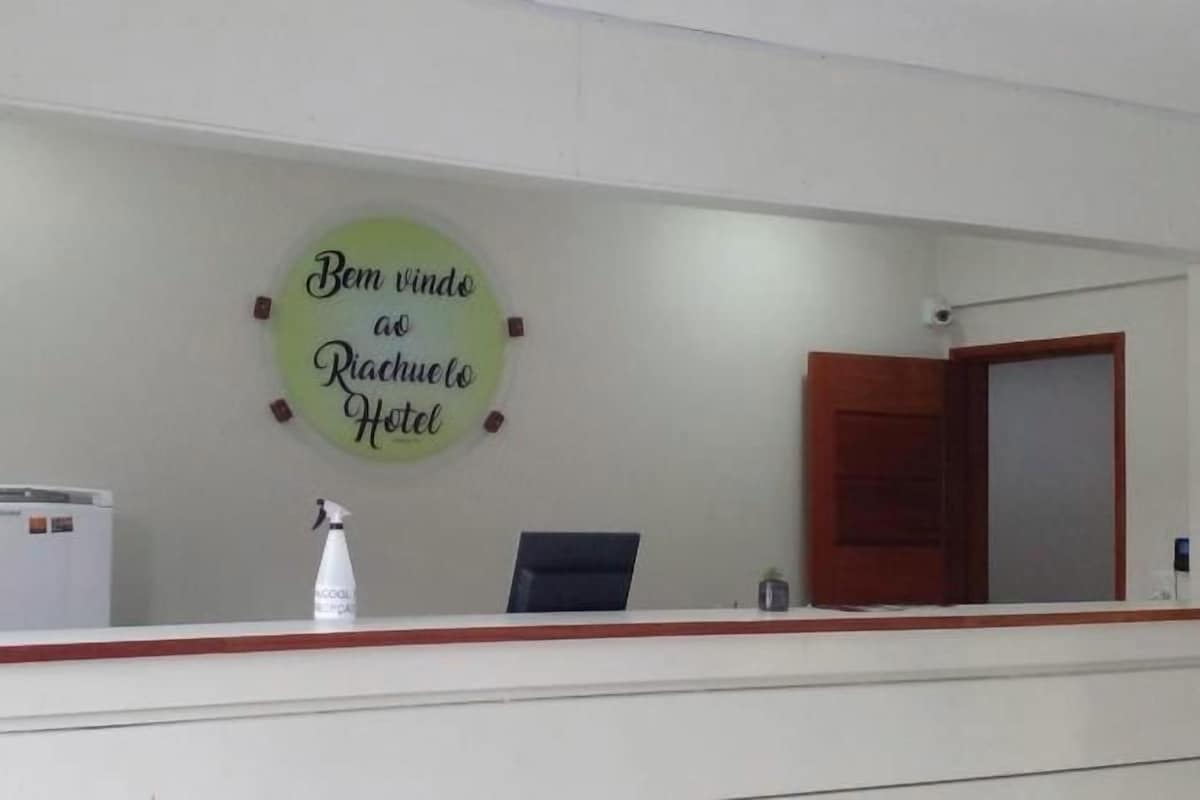 A reception desk with a sign that reads 'Bem vindo ao Rachute Hotel' and a door to the right.