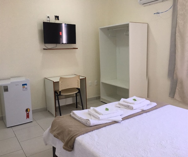 A hotel room with a bed, a desk, a chair, a TV, and a minibar.