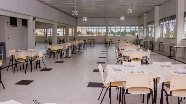 A spacious dining hall with multiple tables and chairs, large windows, and ceiling lights. - Riachuelo Hotel (Resende)
