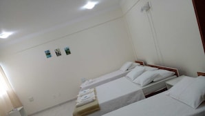 A hotel room with two single beds, a small bedside table, and a wall-mounted light fixture. - Riachuelo Hotel (Resende)
