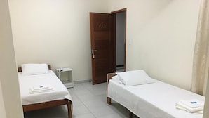 A small, clean room with two single beds, a wooden door, and a white tiled floor. - Riachuelo Hotel (Resende)