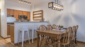 Une cuisine moderne avec des meubles en bois, un îlot central doté de tabourets, une table à manger avec des chaises et un luminaire suspendu.