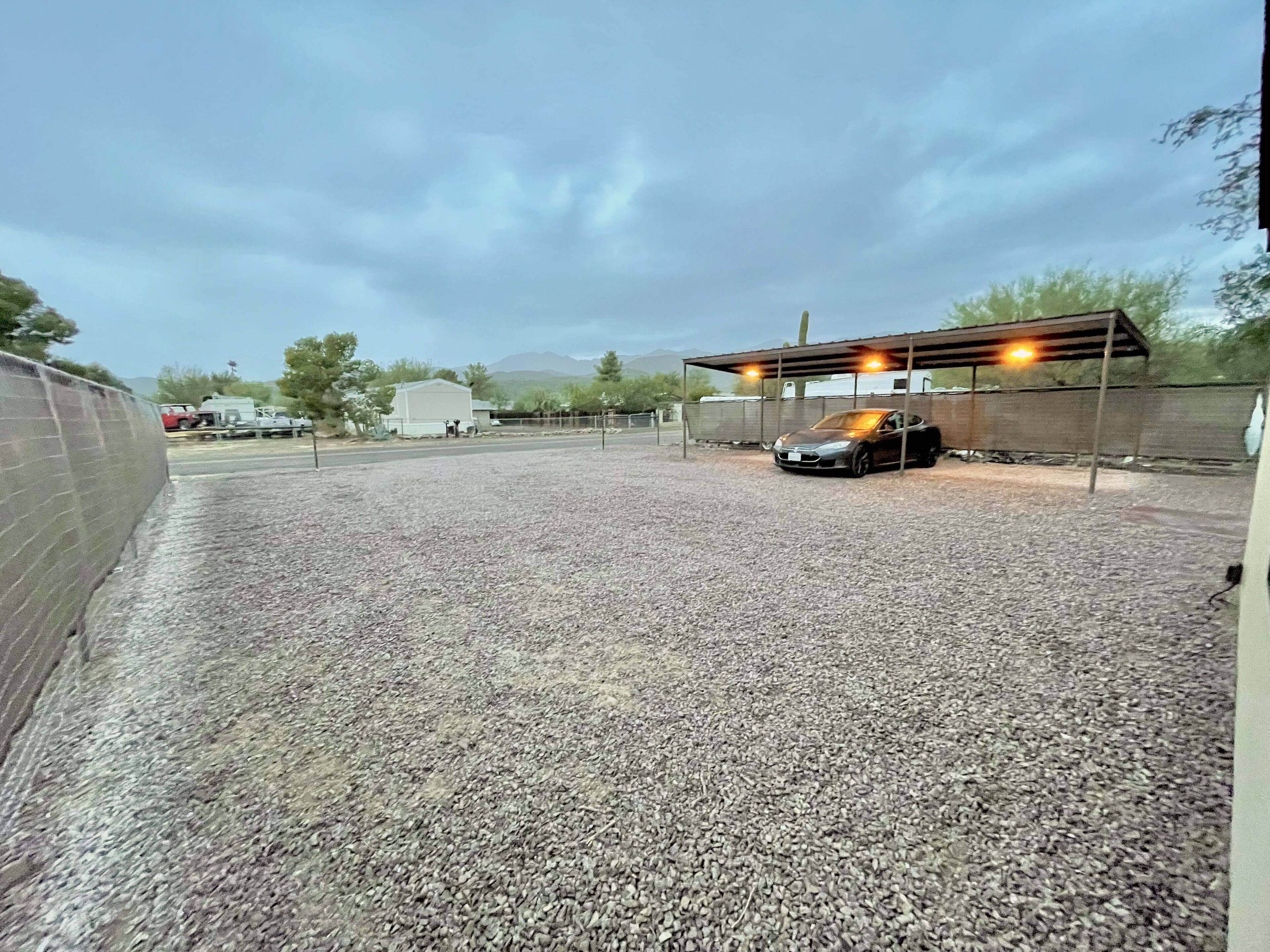 A gravel parking area with a covered carport and a building in the background.