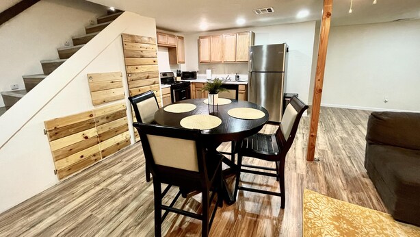 A modern kitchen with wooden cabinets, a stainless steel refrigerator, and a dining area with a round table and chairs.