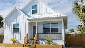 A two-story white house with a wooden front porch, a wooden staircase, and a wooden fence.