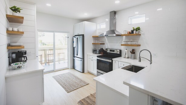 A modern kitchen with white cabinetry, stainless steel appliances, and wooden shelves.