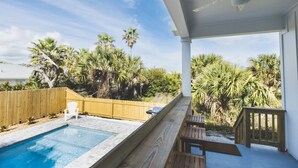 A covered outdoor area with a pool, wooden deck, and palm trees.