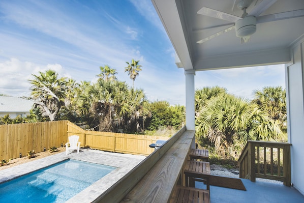 Un espace extérieur abrité comprenant une piscine, une terrasse en bois et des palmiers.