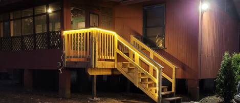 Un edificio de madera con una escalera y una terraza, rodeado de árboles y suelo nevado.