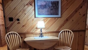 A wooden-paneled room with a round table and two chairs, a framed picture on the wall, and a table lamp. - Toddy's Cabin (Trempealeau)