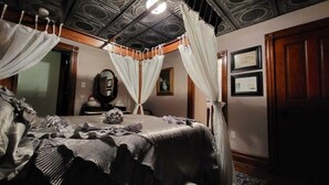 A four-poster canopy bed with a dark, striped bedspread and white drapes. - SWICHBACK TRAIL SUITE AT TRAILS END  B&B (Jim Thorpe)