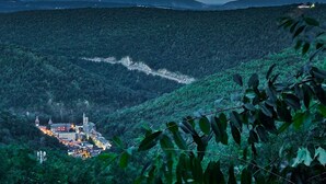A mountainous landscape with a small town nestled in a valley. A road winds through the valley, leading to a cluster of buildings with a prominent church spire. - SWICHBACK TRAIL SUITE AT TRAILS END  B&B (Jim Thorpe)