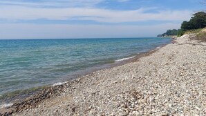 A pebbled beach with clear water and a distant shoreline.