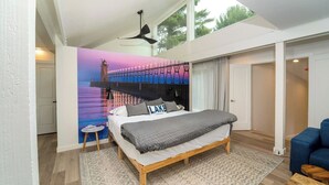 A bedroom with a bed, a nightstand, a ceiling fan, a large window, and a mural of a pier.