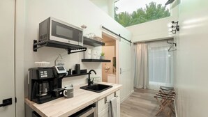 A compact kitchen with a microwave, coffee maker, and sink. There is a small window with a view of trees.