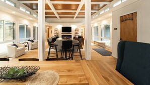 A spacious living area with a wooden ceiling, a dining table with chairs, and a TV in the background.