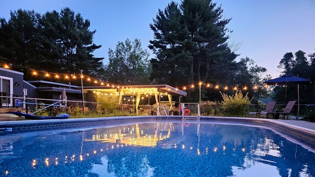 A clear swimming pool with a deck area, surrounded by trees and string lights.