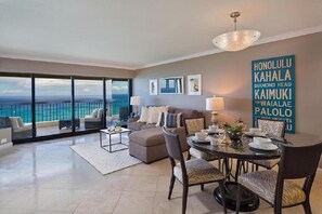 Relax in this spacious living room with a sofa, armchairs, and dining table for four, leading to a balcony with ocean views.
