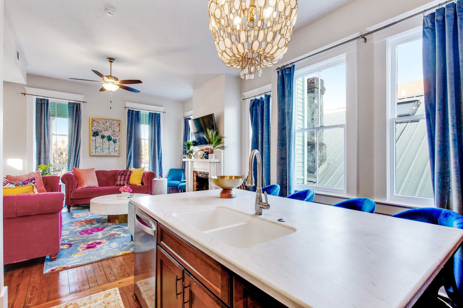 A modern kitchen with a central island, a dining area with blue chairs, and a living room with a red sofa.