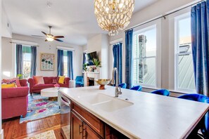 A modern kitchen with a central island, a dining area with blue chairs, and a living room with a red sofa.