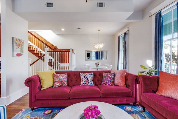 A spacious living room with a large red sofa, a white coffee table, and a staircase leading to a dining area.