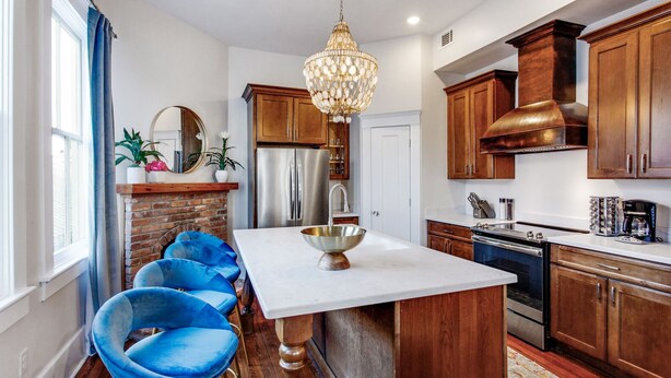 Una cocina moderna con una isla central, armarios de madera, electrodomésticos de acero inoxidable y sillas azules.
