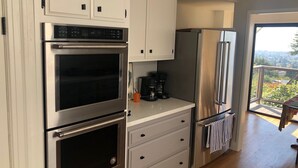 Una cucina moderna con elettrodomestici in acciaio inossidabile, mobili bianchi e vista su un balcone con panorama urbano.