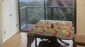 Zona pranzo con tavolo apparecchiato per due, una sedia e vista sulla città attraverso ampie finestre.
