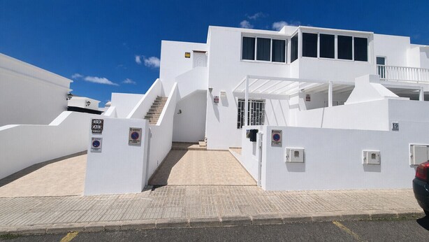 A white building with a staircase leading to a balcony, a parking area, and a clear blue sky. - Casa Donna" | Holiday Home in Lanzarote - Spain (Playa Honda)