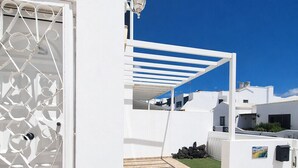 A white building with a decorative metal gate, a tiled patio, and a clear blue sky. - Casa Donna" | Holiday Home in Lanzarote - Spain (Playa Honda)