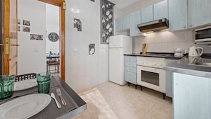 A compact kitchen with light blue cabinets, a white refrigerator, a stove, and a microwave. There is a dining table with green glasses and cutlery. - Casa Donna" | Holiday Home in Lanzarote - Spain (Playa Honda)
