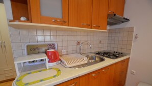 A kitchen with wooden cabinets, a sink, a stove, and a coffee maker. - Jela studio apartment (Rovinj)