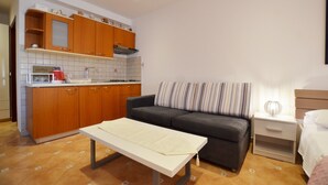 A compact living space with a kitchenette, a sofa, a small table, and a bedside table with a lamp. - Jela studio apartment (Rovinj)
