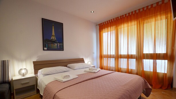 A neatly made bed with a pink bedspread, a nightstand with a lamp, and a framed picture of the Eiffel Tower on the wall. - Jela studio apartment (Rovinj)