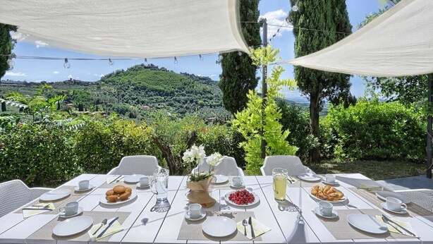 Un espace de restauration en plein air, avec des tables dressées pour le repas, entouré de verdure et offrant une vue sur un paysage vallonné.