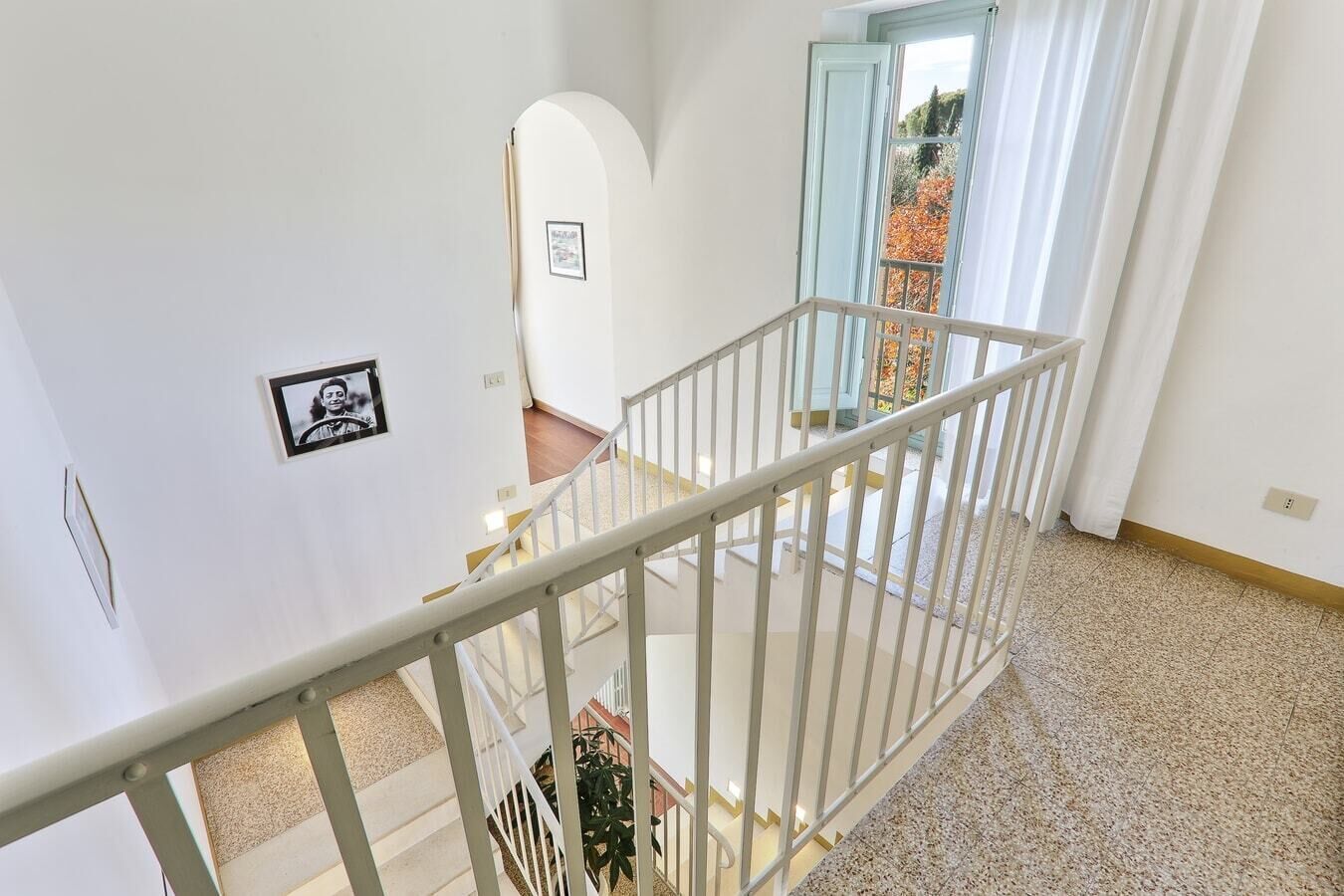 Eine Treppe mit weißer Geländer führt zu einer Empore. An der Wand befinden sich Bilder in Rahmen und eine Tür, die nach draußen führt.