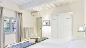 Une chambre d’hôtel avec un lit, un radiateur, un panier contenant des serviettes, une lampe et une armoire dont les portes sont étiquetées « Deauville », « Saint-Malo » et « Cabourg ».