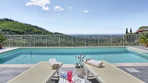 Une piscine avec deux chaises longues, une serviette et un verre d’eau sur la terrasse.