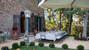 An outdoor dining area with a long table set for a meal, surrounded by potted plants and trees.