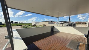 An outdoor deck with a wooden floor, metal railings, and a covered area with a view of the surrounding landscape.