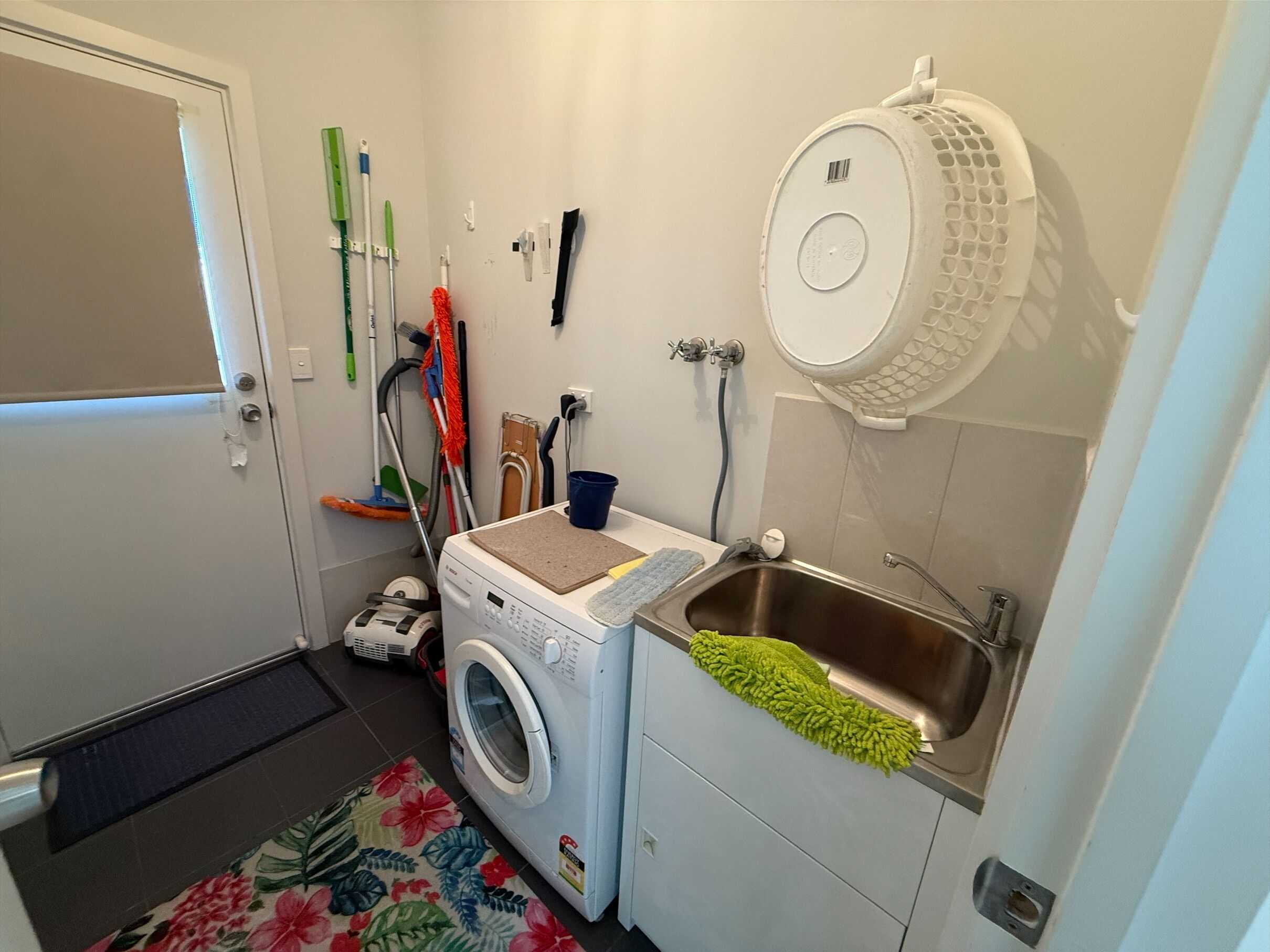 A compact laundry room with a washing machine, a sink, and various cleaning tools.